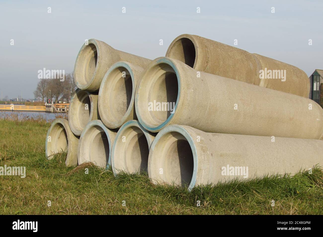 Palo di tubi fognari di calcestruzzo nell'erba. Sullo sfondo il canale chiamato Noordhollandsch kanaal. Olanda, Olanda del Nord, novembre. Foto Stock