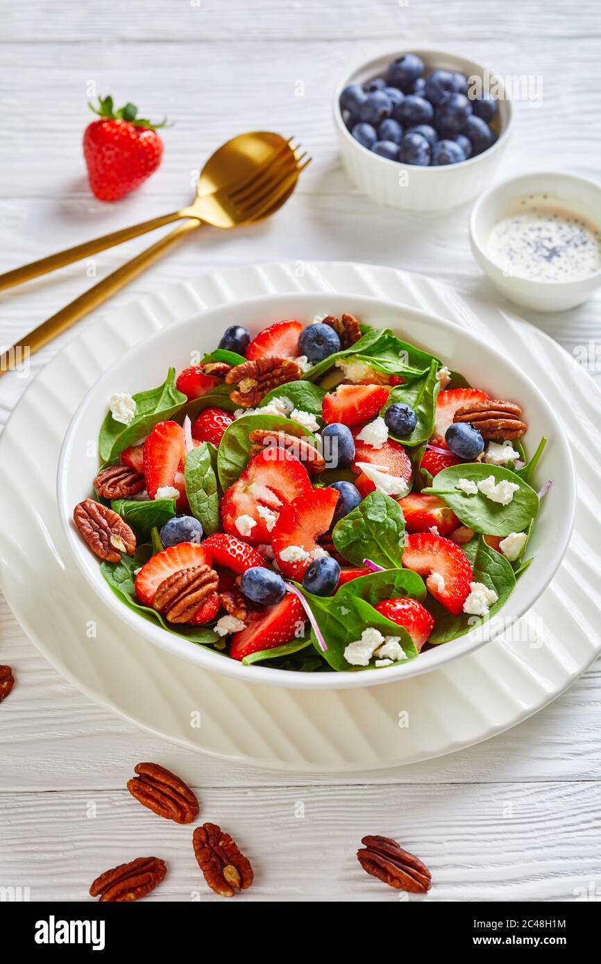 insalata estiva di spinaci al mirtillo con noci pecan e formaggio feta sbriciolato in una ciotola bianca su un tavolo di legno, vista verticale dall'alto Foto Stock