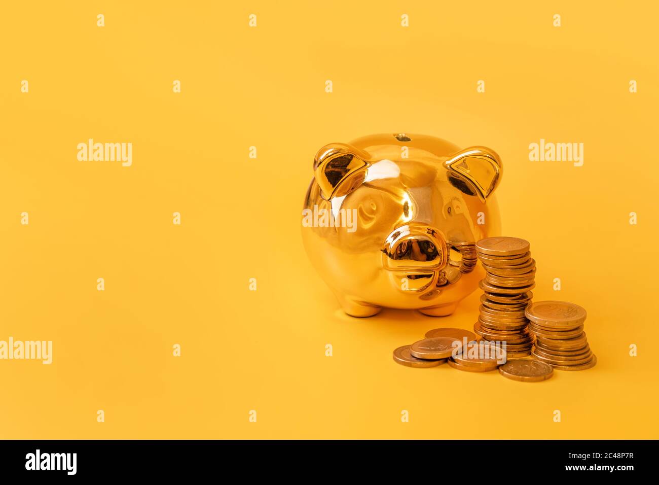 Golden piggy banca con torri di denaro su sfondo giallo. Pila di monete in euro vicino al contenitore di denaro dorato. Denaro maiale, risparmio di denaro, Moneybox, finanza e. Foto Stock