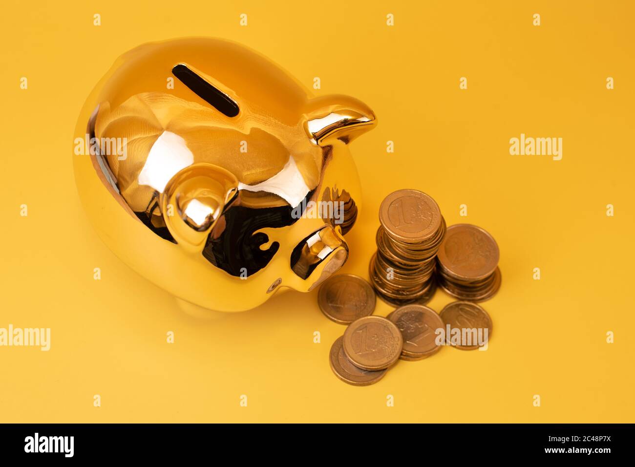 Golden piggy banca con torri di denaro su sfondo giallo. Pila di monete in euro vicino al contenitore di denaro dorato. Denaro maiale, risparmio di denaro, Moneybox, finanza e. Foto Stock