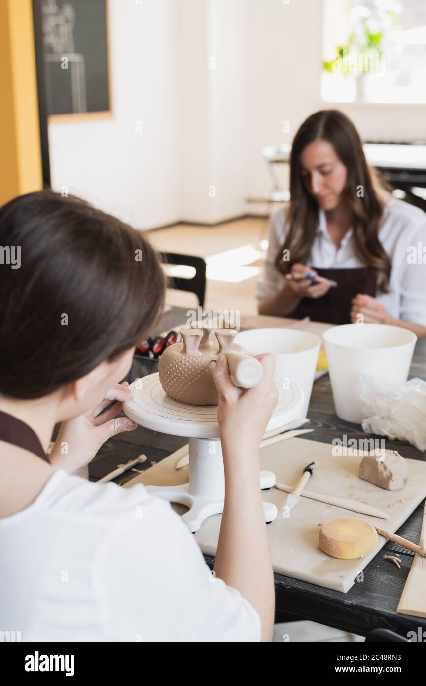 Primo piano del fondo della tazza, che è in fase di decorazione in studio di ceramica. Le mani professionali femminili che fanno i punti o le gocce di creta sulla superficie di vaso vicino Foto Stock