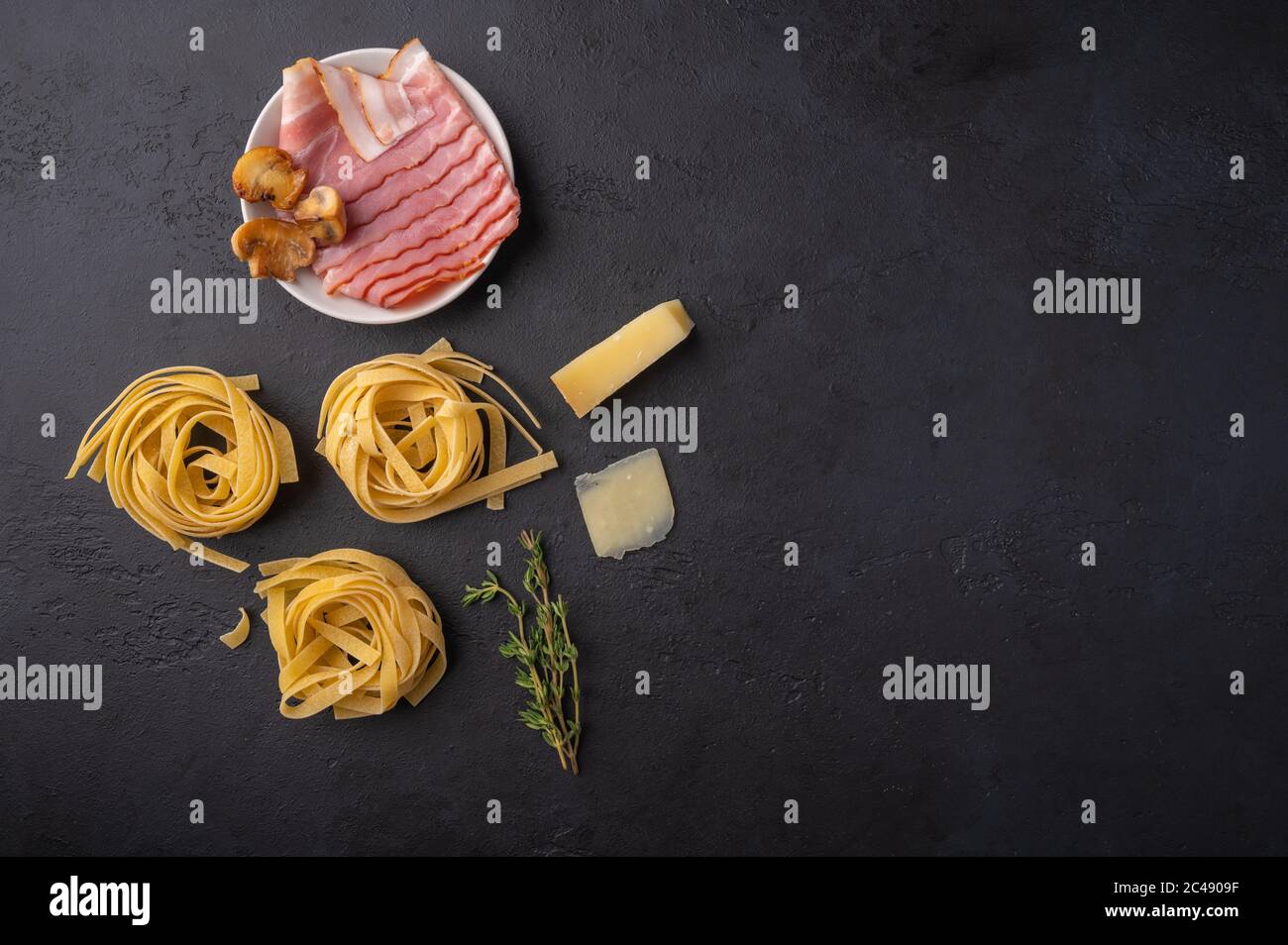 Vista dall'alto ingredienti di pasta fettuccine con funghi, pancetta e parmigiano. Cibo grezzo su sfondo di grafite scuro con spazio di copia Foto Stock