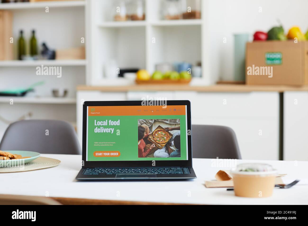 Computer portatile con sito web di consegna del cibo sullo schermo sul tavolo in cucina Foto Stock