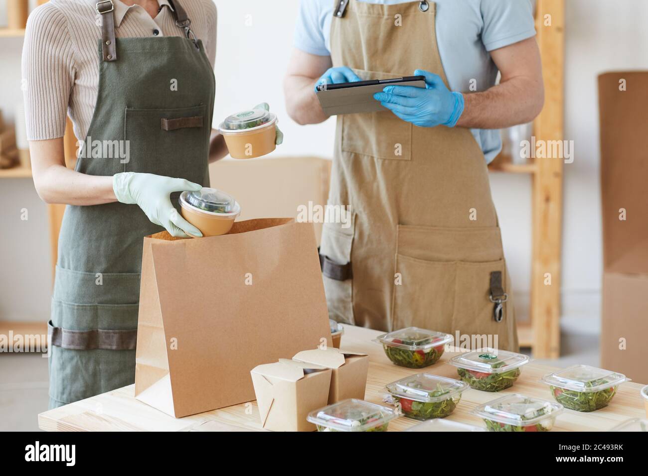Primo piano di due lavoratori in guanti protettivi che lavorano nel servizio di consegna imballano il cibo in sacchetti di carta Foto Stock
