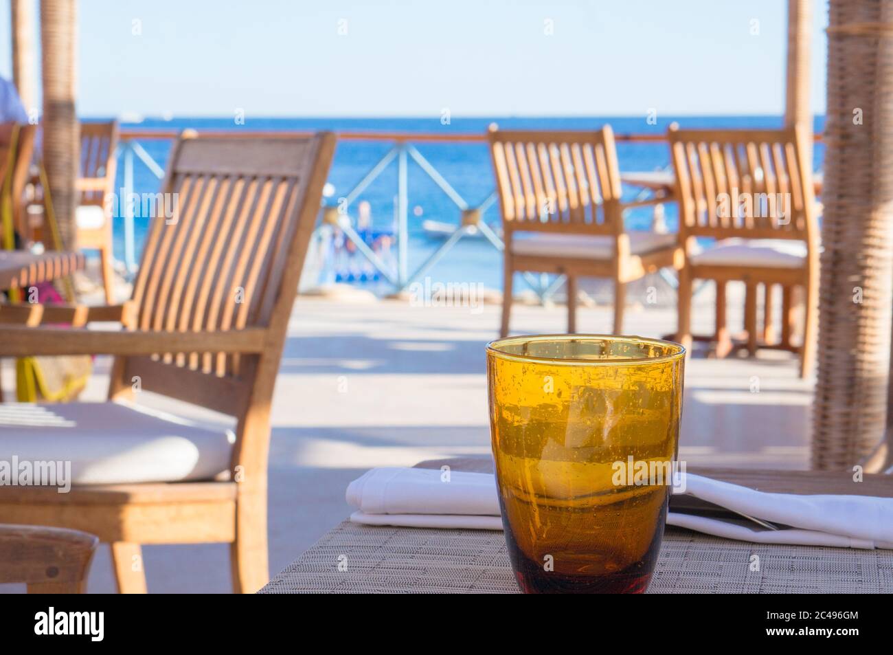 Un vetro arancione vuoto che si erge sul tavolo presso il Beach cafe con vista mare Foto Stock