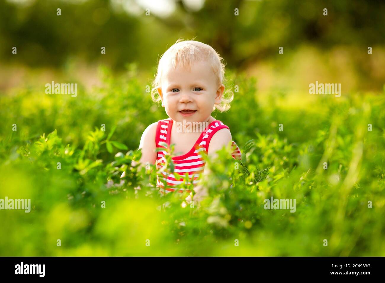 Carina bambina sorridente in rosso estate vestito a piedi sul prato verde Foto Stock