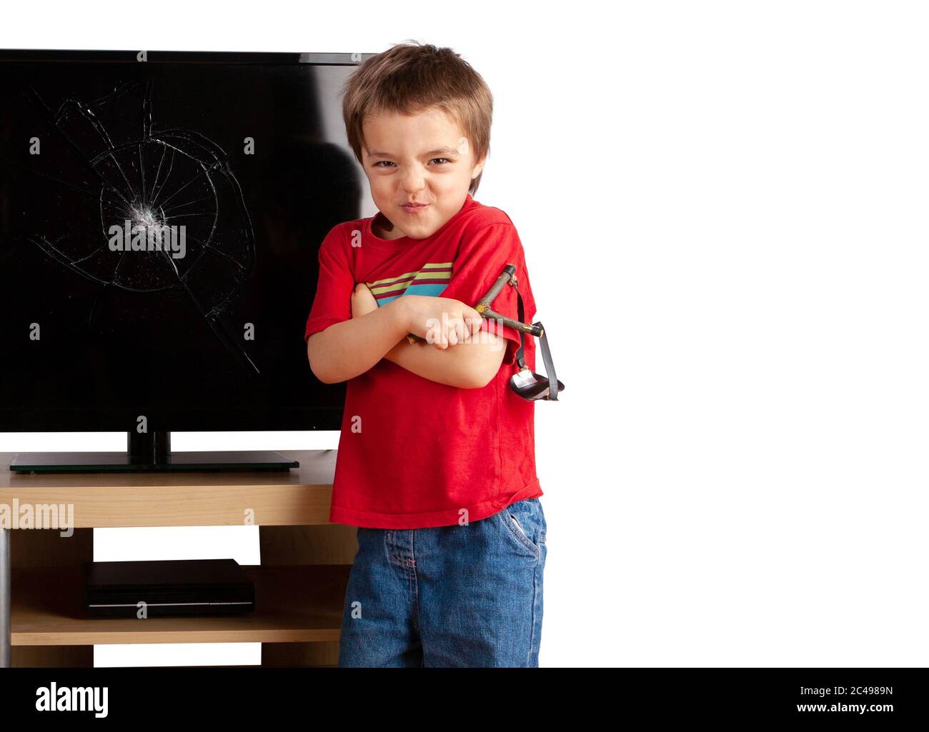 Naughty piccolo ragazzo che tiene una foto di schianto in piedi davanti a un televisore con schermo rotto Foto Stock