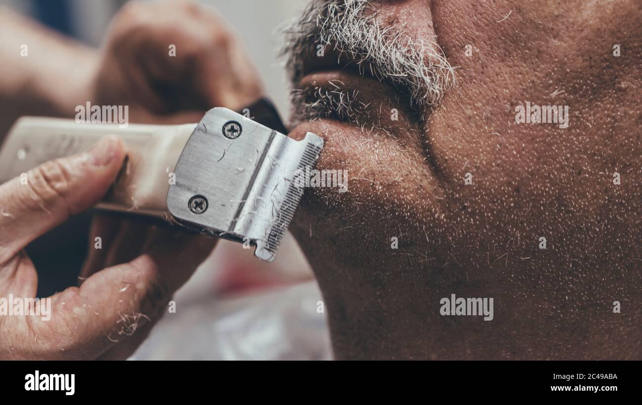 Primo piano di rasoio elettrico che è nelle mani di un barbiere.Serious  master barba da taglio del cliente anziano nel salone Foto stock - Alamy