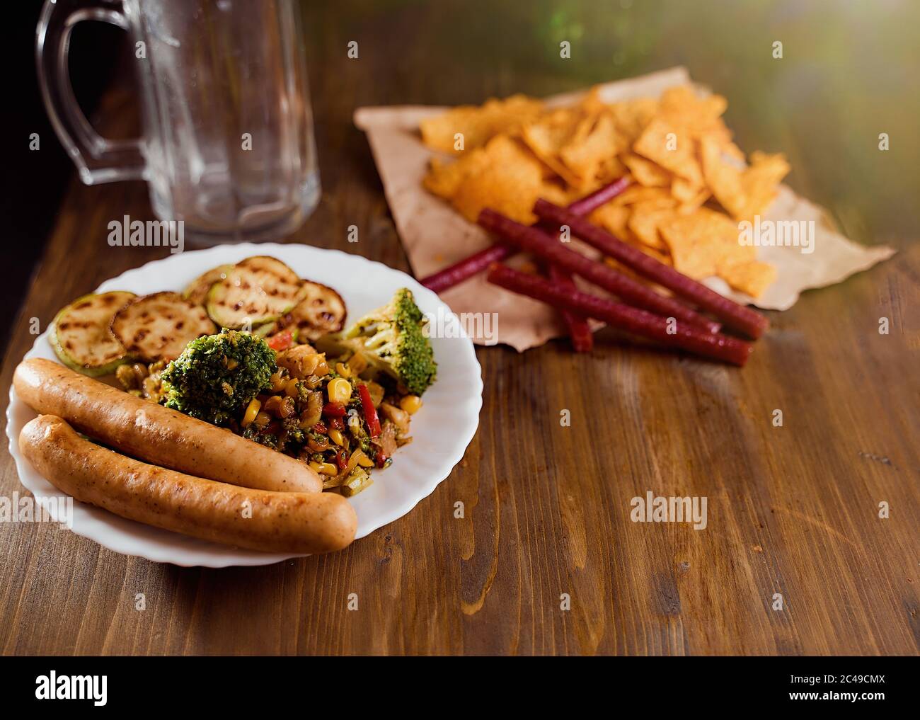 Verdure alla griglia con salsiccia e nachos di mais messicani si trovano su un tavolo di legno. Una cosa in un recipiente con salsa. Con spazio per la copia Foto Stock