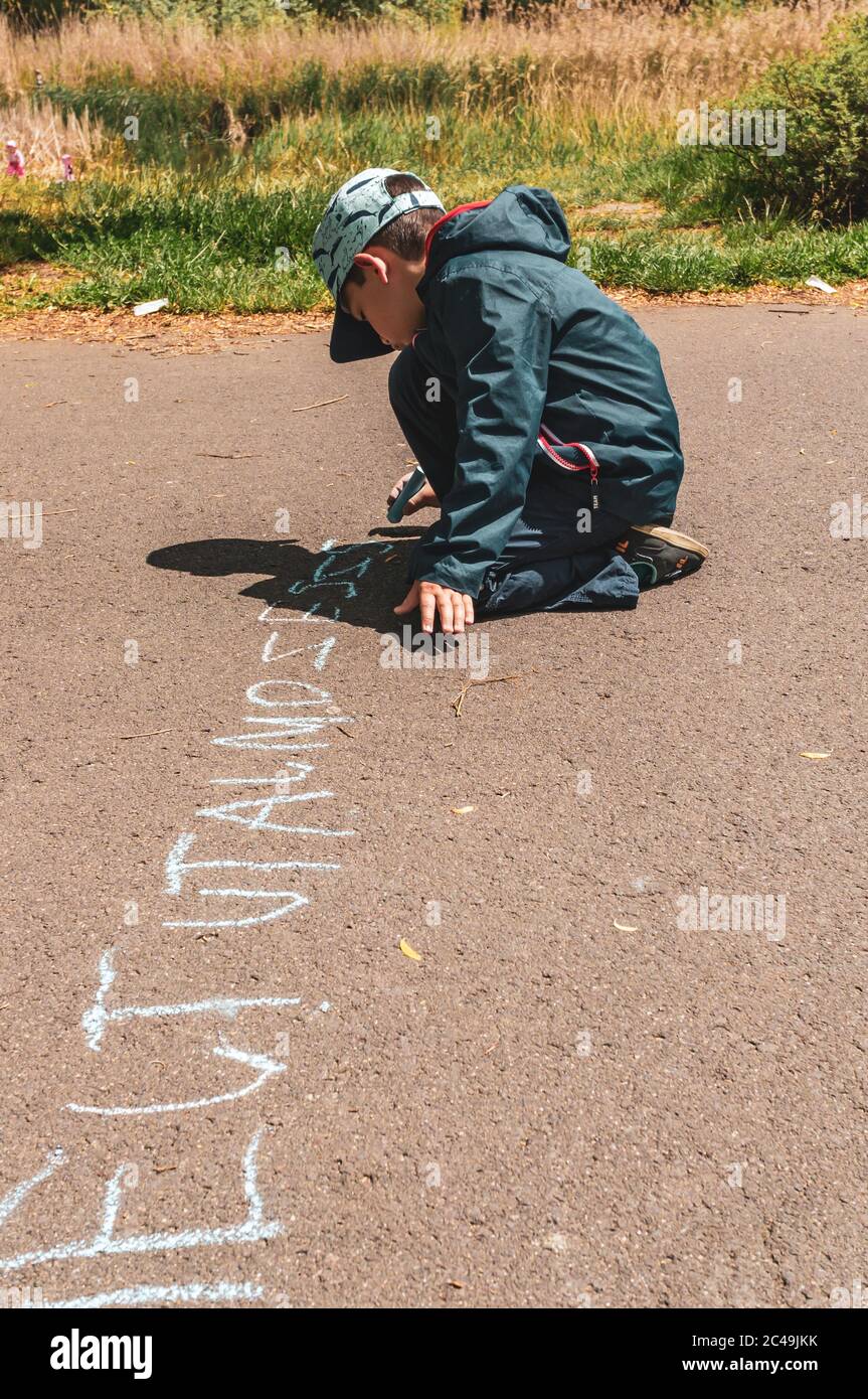 POZNAN, POLONIA - 30 maggio 2020: Ragazzo caucasico polacco di sei anni che scrive con il pastello su un sentiero nel parco Jan Pawla Foto Stock