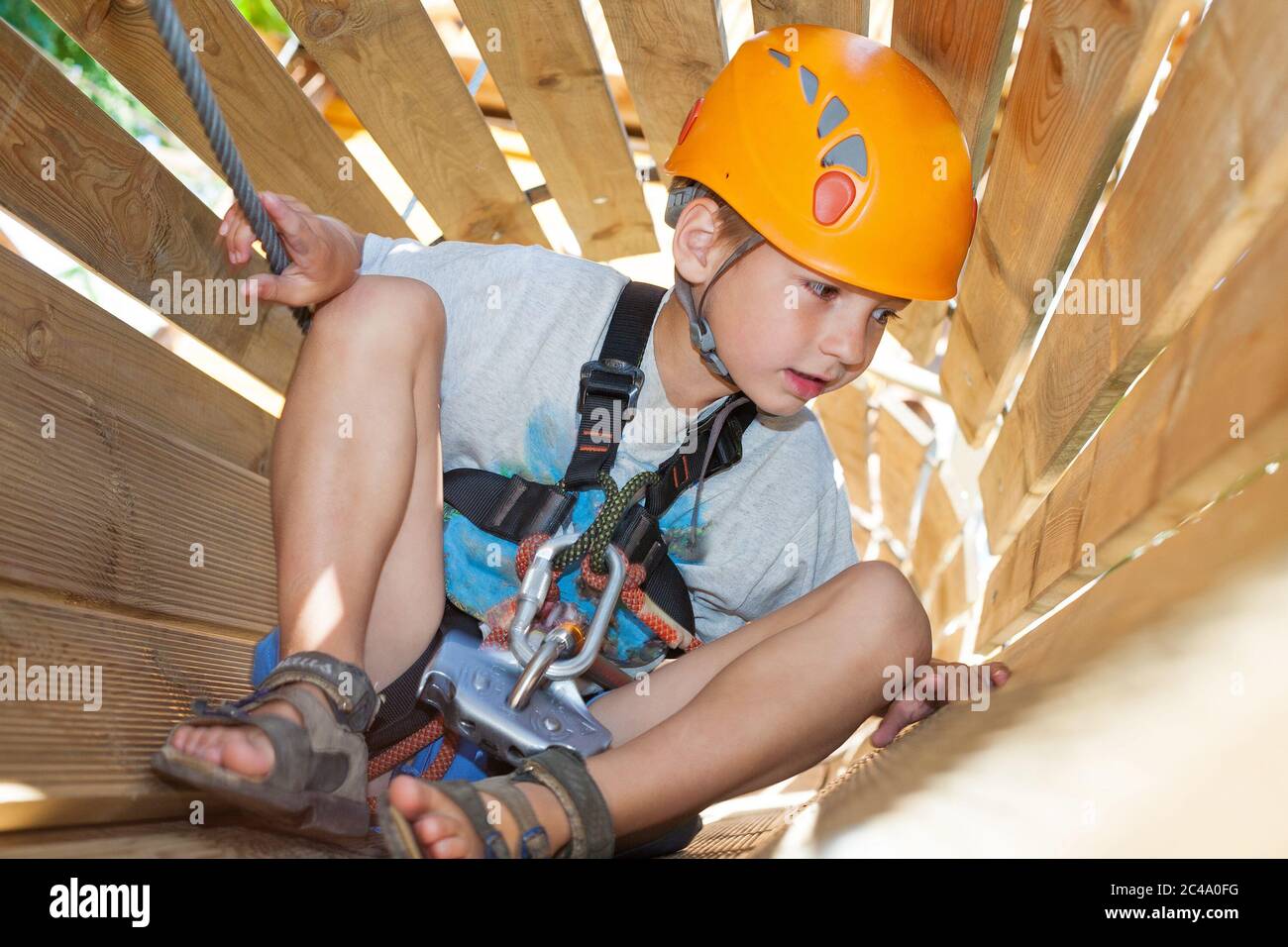 Ragazzo carino con attrezzatura da arrampicata in un parco avventura in un tunnel di legno Foto Stock