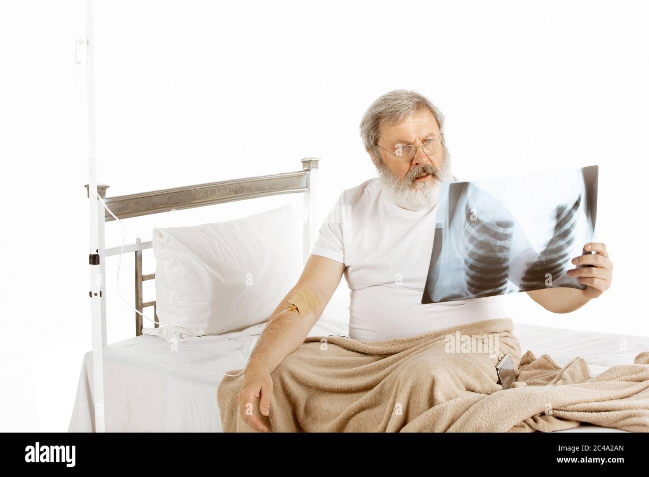 Anziano anziano che si ritrova in un letto d'ospedale isolato su sfondo bianco. Ottenere la cura. Concetto di salute e medicina. Primo piano con IV per il trattamento, guardando la scansione polmonare. CopySpace. Foto Stock