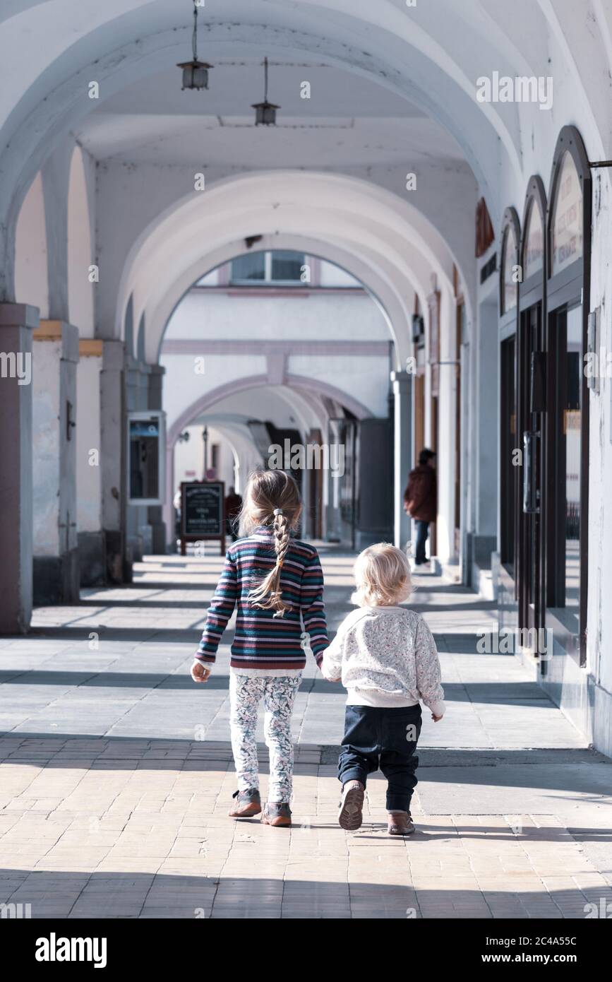 Due bambini camminano insieme a mano nella vecchia strada porticata della città. Amore di famiglia e tema di amicizia. Foto Stock