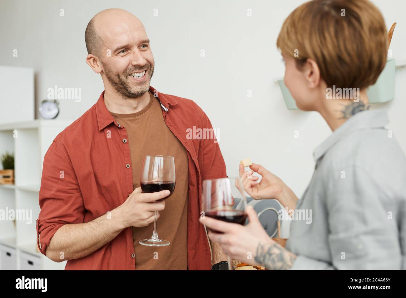 Uomo maturo sorridente e che parla con la donna mentre degustano vino rosso con formaggio Foto Stock
