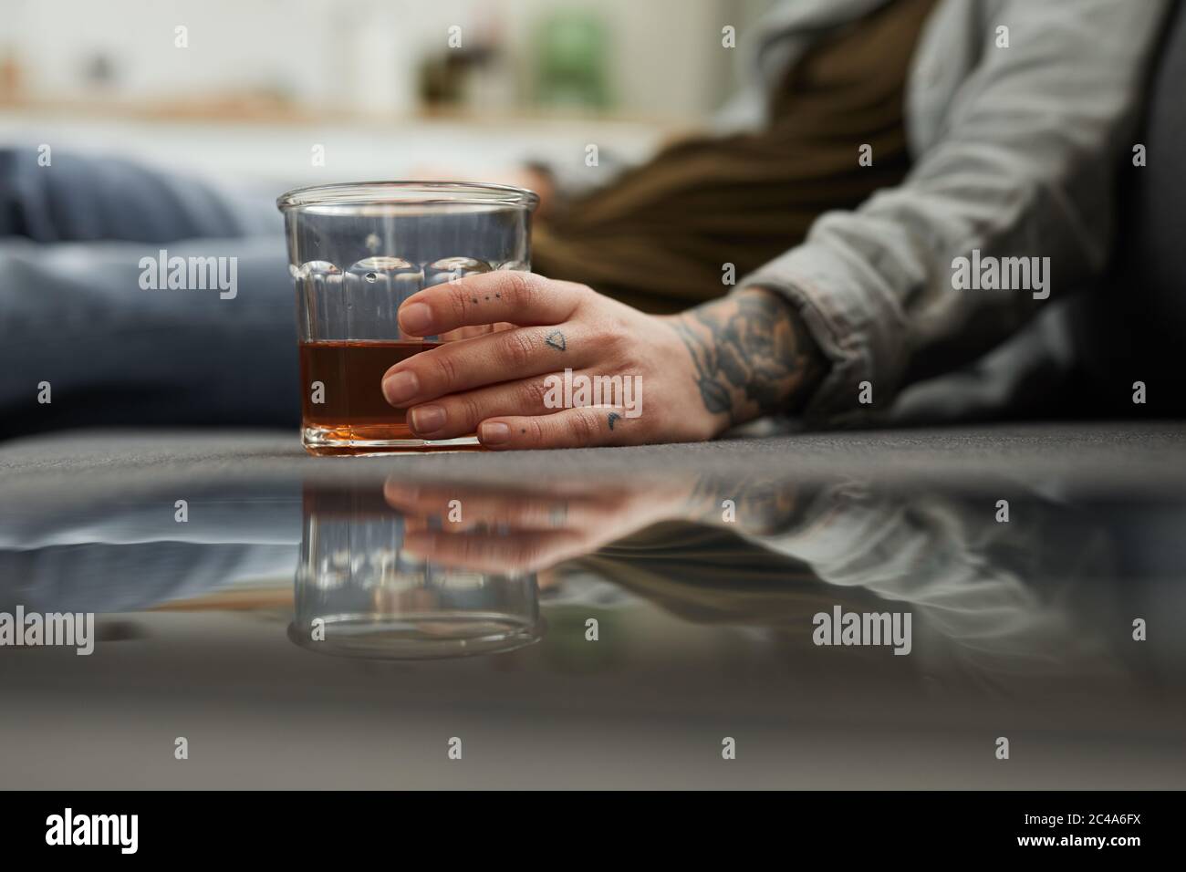 Primo piano di giovane donna con bicchiere di whisky seduto a terra e bevendo a casa Foto Stock
