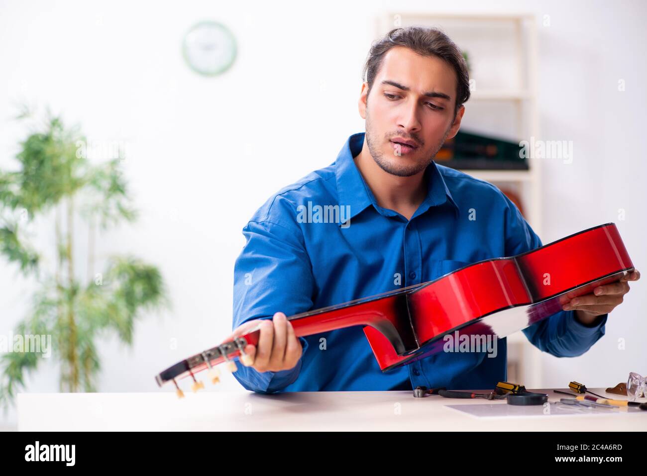 Giovane uomo riparatore riparando la chitarra Foto Stock