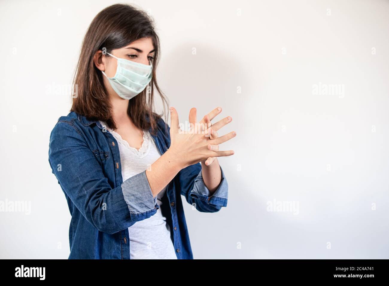 Donna con maschera di protezione medica che mette su antisettico per disinfettare le mani Foto Stock