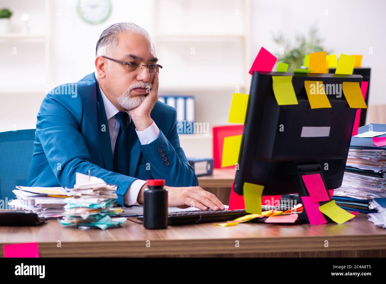 Vecchio dipendente che lavora in ufficio in un concetto di priorità contrastanti Foto Stock