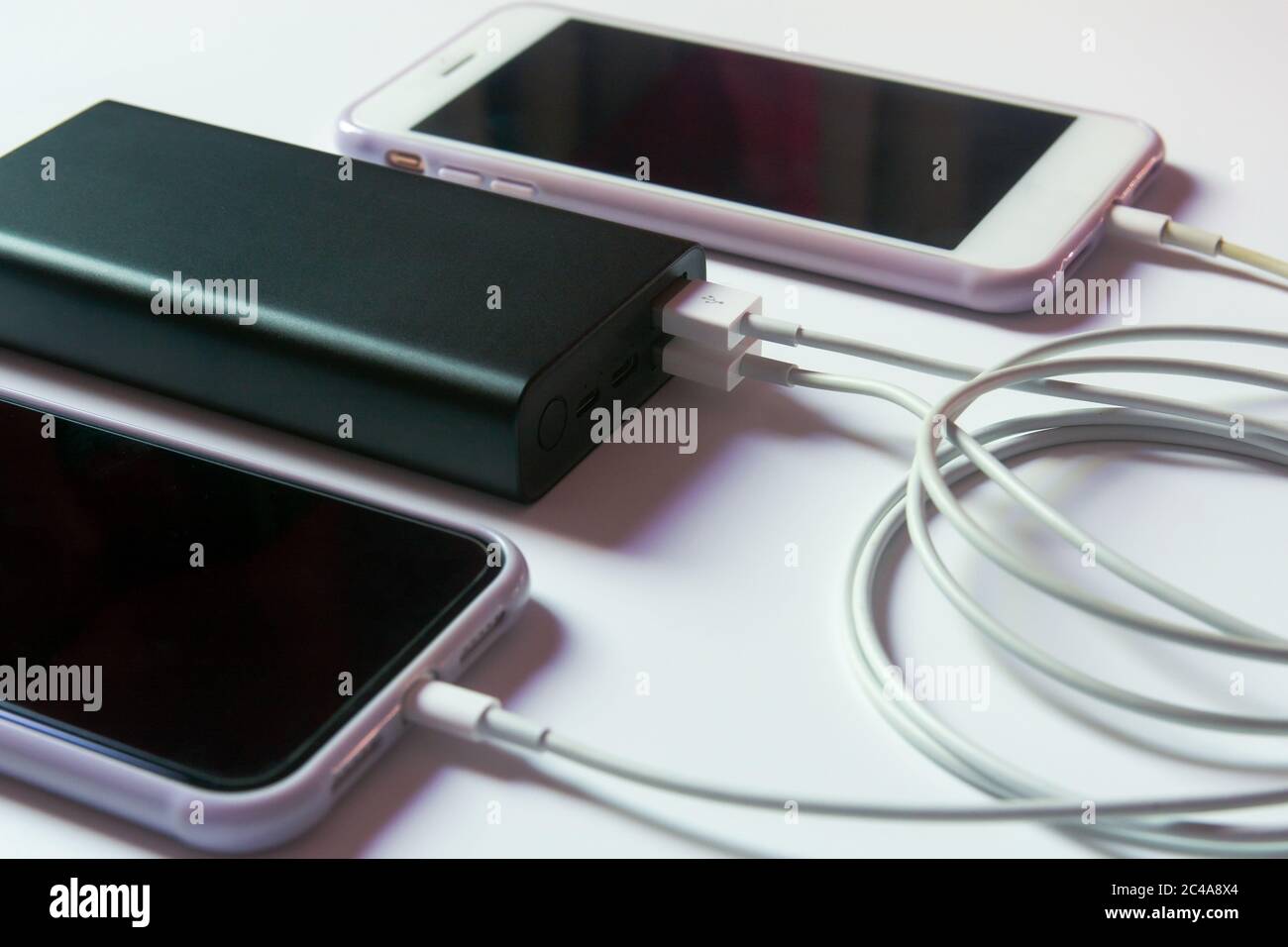 Ricarica dello smartphone con power bank su una scrivania bianca Foto Stock