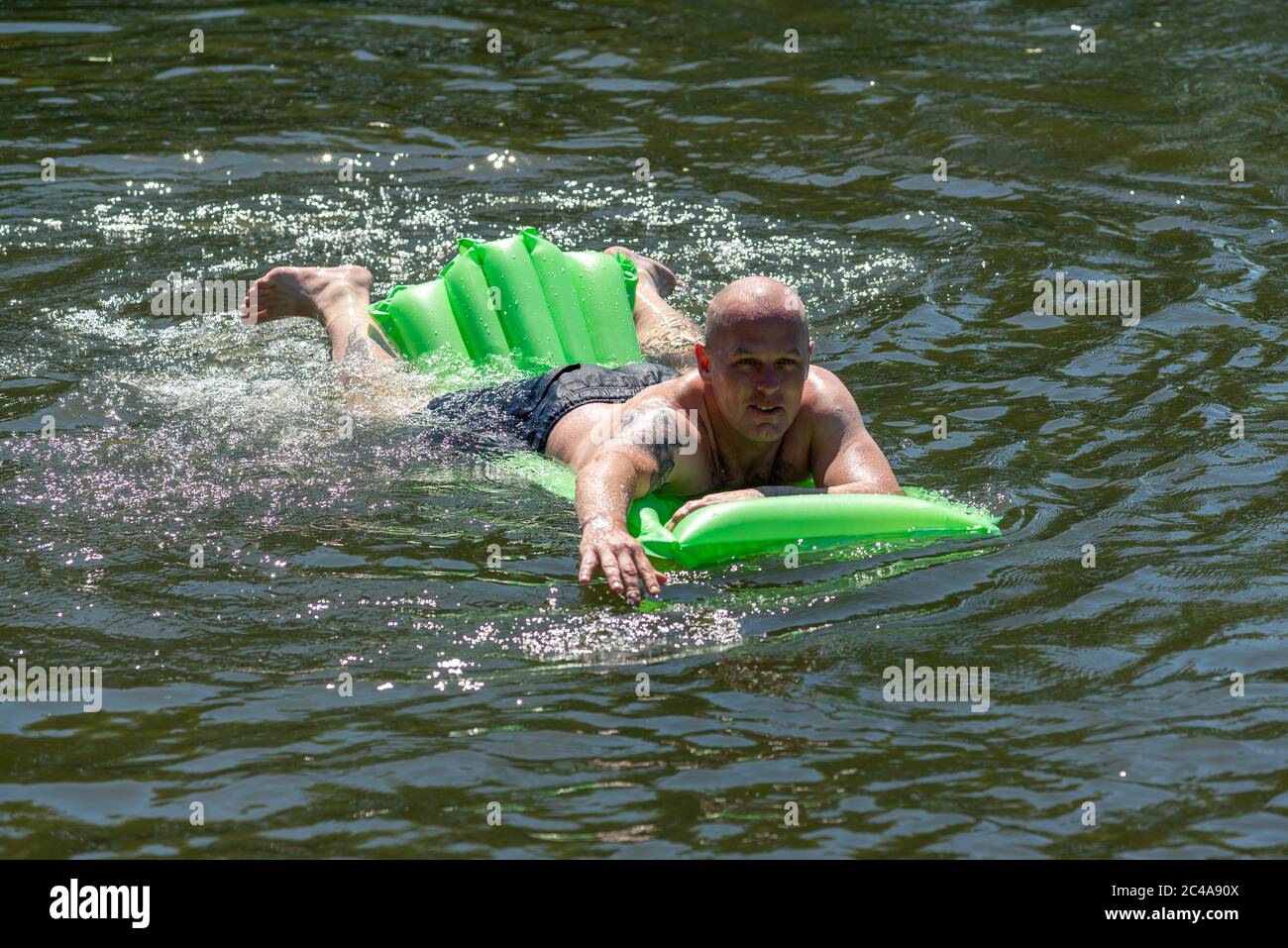 Uomo su un lilo che nuota nel fiume Avon rinfrescarsi nell'acqua fredda. L'onda di calore di metà estate lo rende la giornata più calda con i più alti livelli di UV finora quest'anno e la temperatura a circa 33 gradi nel pomeriggio. Fordingbridge, New Forest, Hampshire, Inghilterra, Regno Unito, 25th giugno 2020. Foto Stock