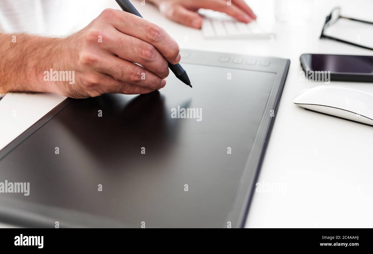 primo piano di una persona che utilizza il tablet e lo stilo per il disegno digitale sulla scrivania da ufficio bianca Foto Stock