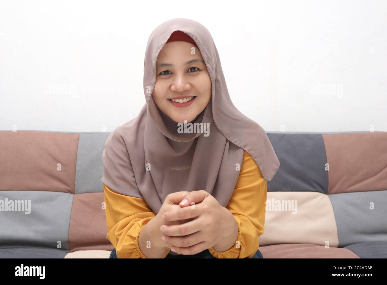 Bella donna musulmana asiatica facendo selfie ritratto al telefono o facendo videochiamata mentre si siede sul divano, felice sorridente espressione allegra Foto Stock