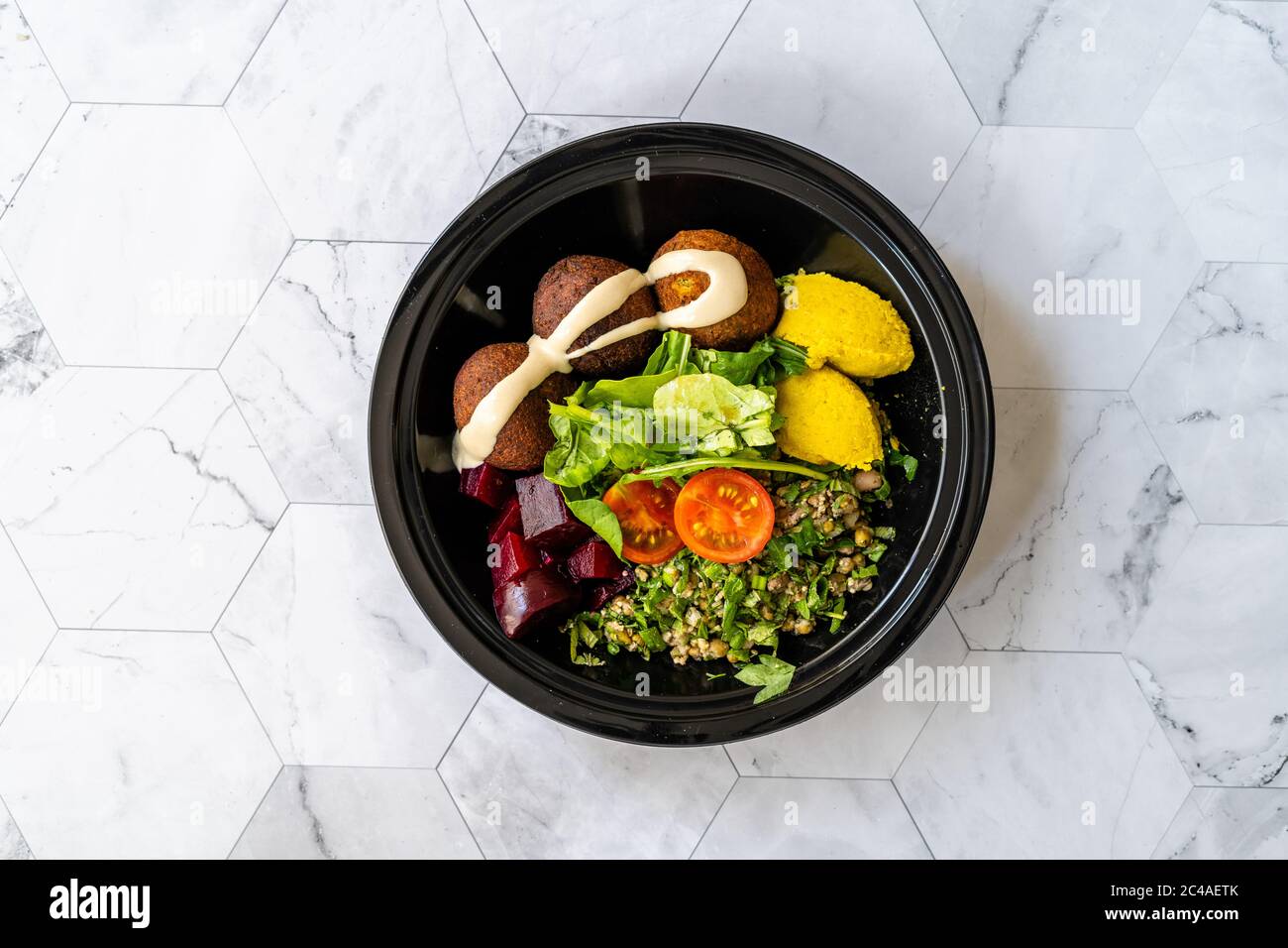 Piatto di Falafel da take away con insalata di fagioli Mung, legume, barbabietola arrosto e salsa di tahini di Hummus giallo in tazza nera di plastica Foto Stock