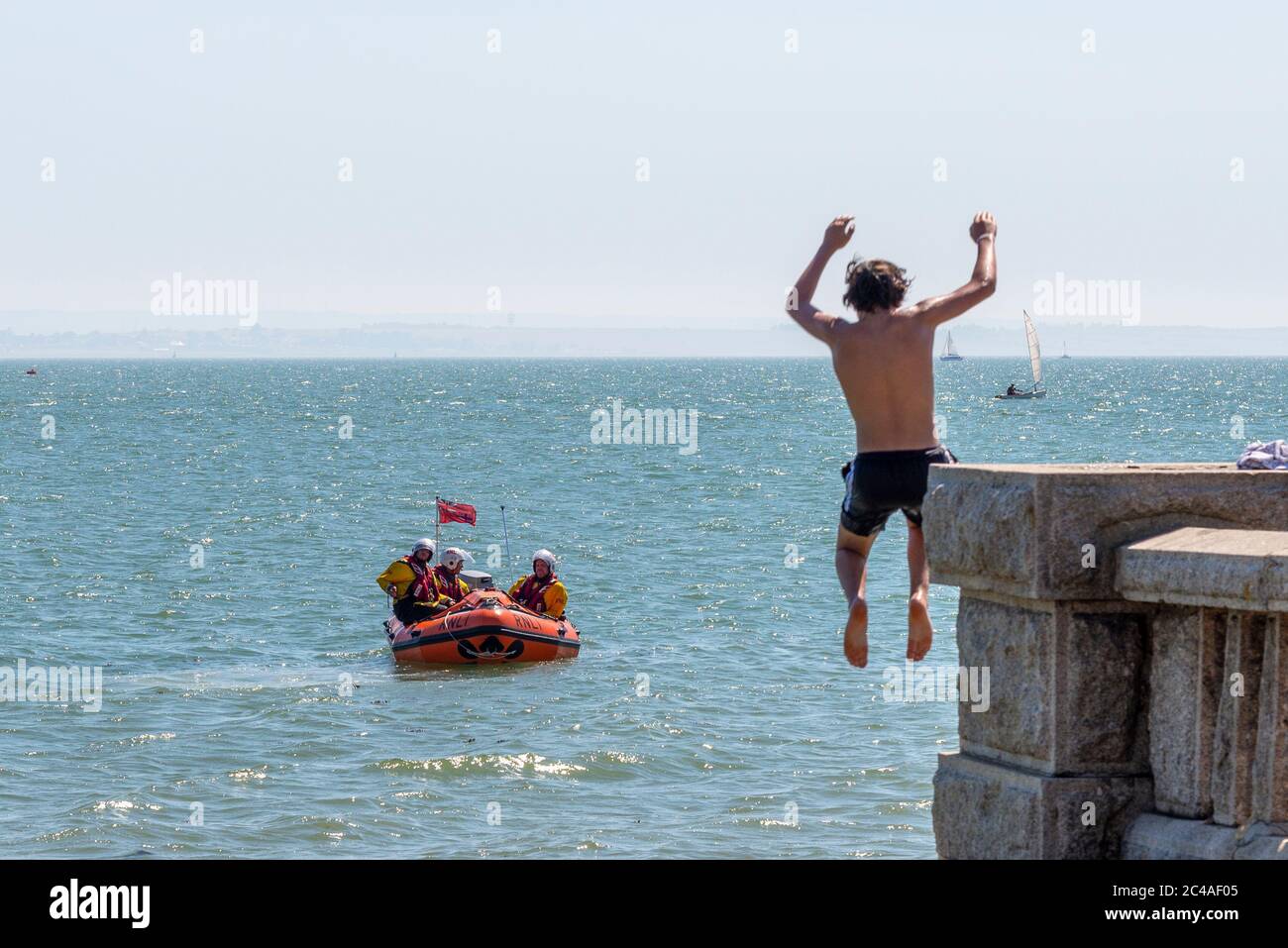 Southend on Sea, Essex, Regno Unito. 25 Giu 2020. Con le previsioni temperature record per 2020 persone si stanno dirigendo verso il lungomare per raffreddare, nonostante il COVID-19 Coronavirus consulenza. A Southend on Sea la riva dell'estuario del Tamigi è piena di persone che nuotano e saltano in mare. Tomblaoning maschile caucasico bianco in mare con l'equipaggio di bagnino RNLI Foto Stock