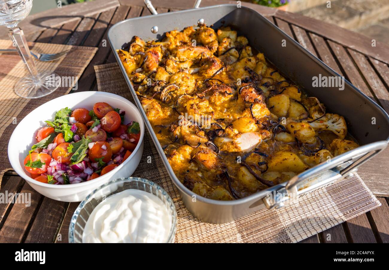 Pollo Aloo Gobi curry servito in vassoio di lattina arrosto cuocere per cena all'aperto con pomodoro e menta chutney e yogurt al sole, Regno Unito Foto Stock