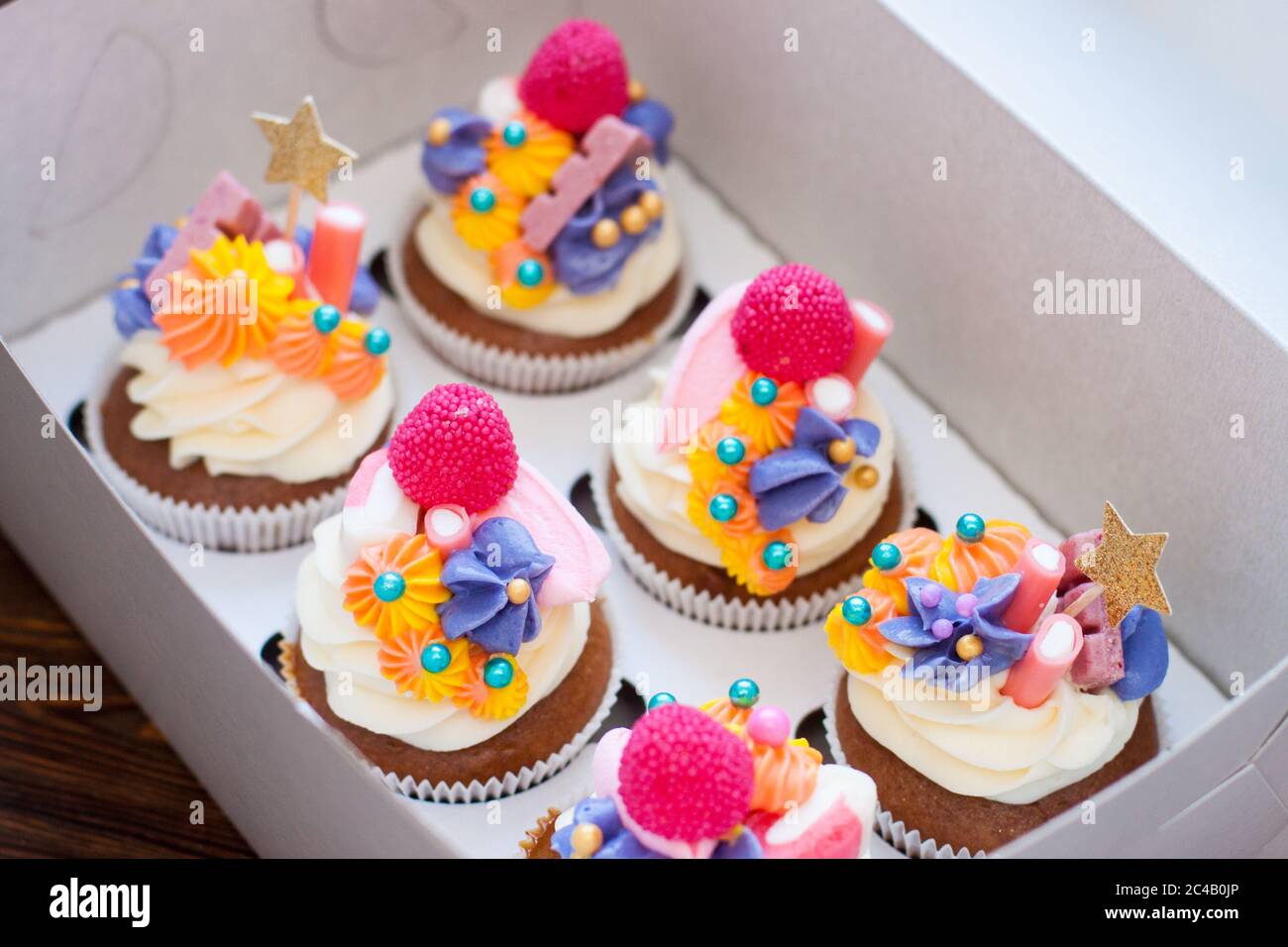 Cupcake natalizi al cioccolato con decorazione di formaggio color crema rosa, stelle dorate, caramelle e marshmallow in scatola regalo. Foto Stock