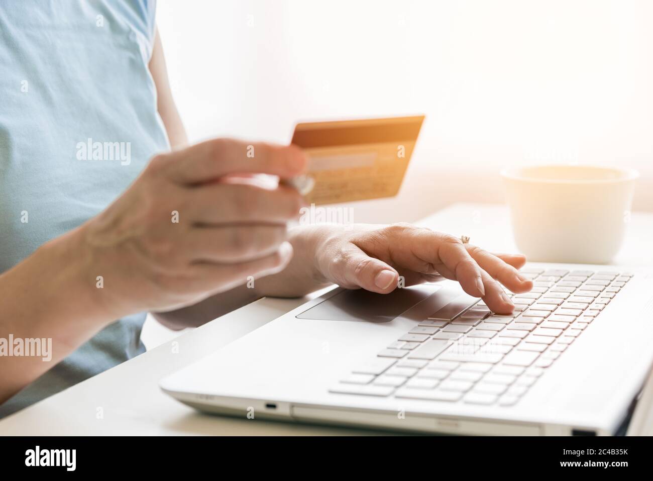 Donna che tiene una carta di credito mentre usa un laptop per l'acquisto online da casa Foto Stock