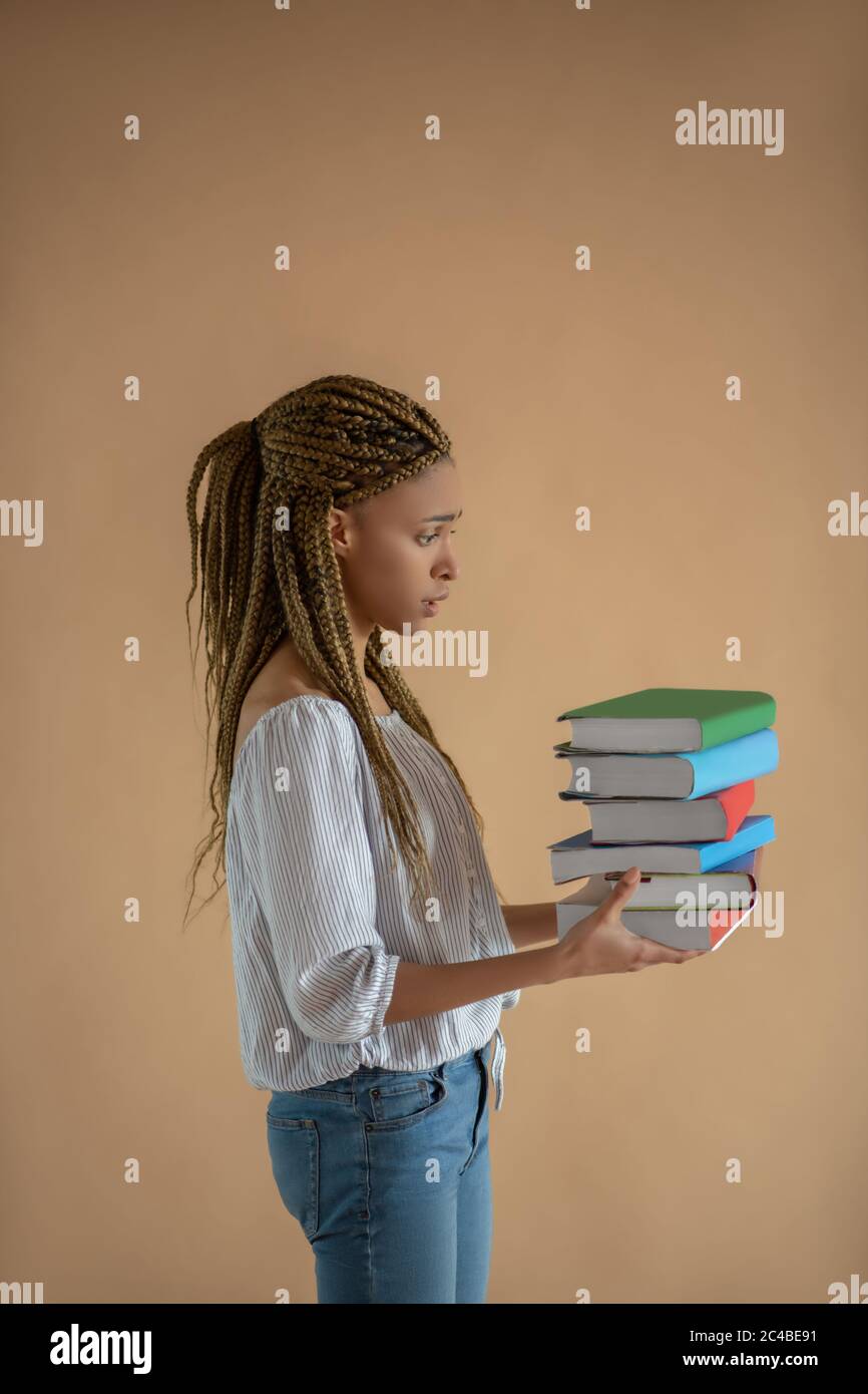 Deluso giovane afroamericana femmina portando mucchio di libri davanti a lei Foto Stock