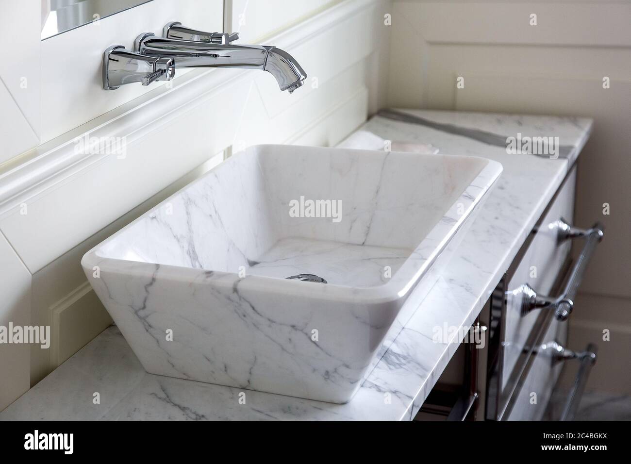 rubinetto cromato con lavabo in marmo bianco e piano di lavoro in bagno con pareti in legno, dettagli ravvicinati. Foto Stock