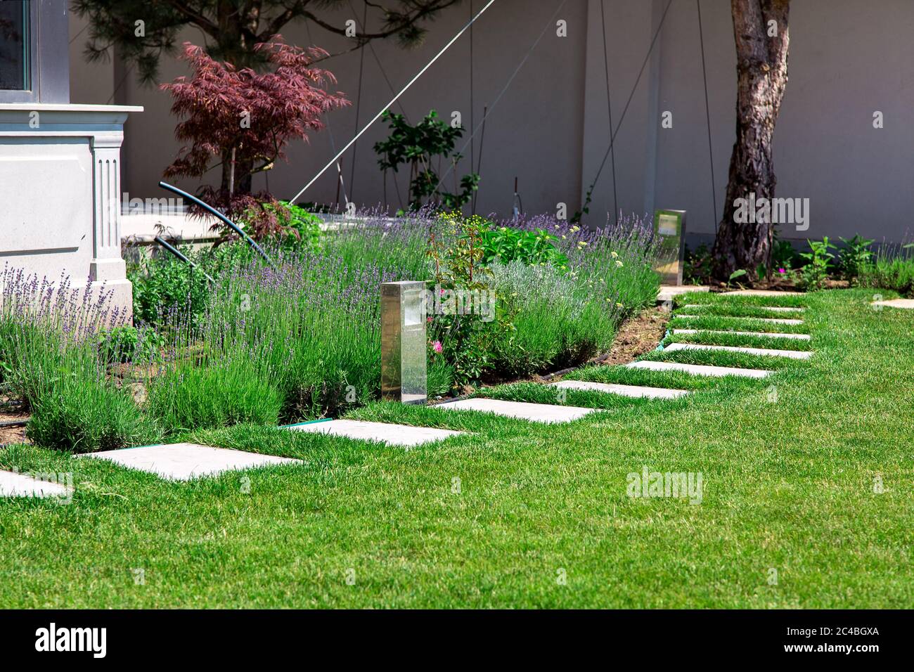 cortile di un palazzo di lusso con un letto fiorito e un percorso in pietra fatto di piastrelle di marmo quadrato in erba verde in una giornata estiva soleggiata. Foto Stock