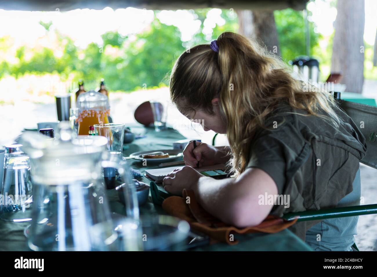 13 anni ragazza che scrive nel suo giornale, campo tended, Botswana Foto Stock