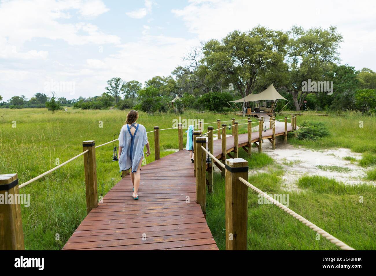 Ragazza di 13 anni che cammina su un sentiero in legno, campo tenda, Botswana Foto Stock