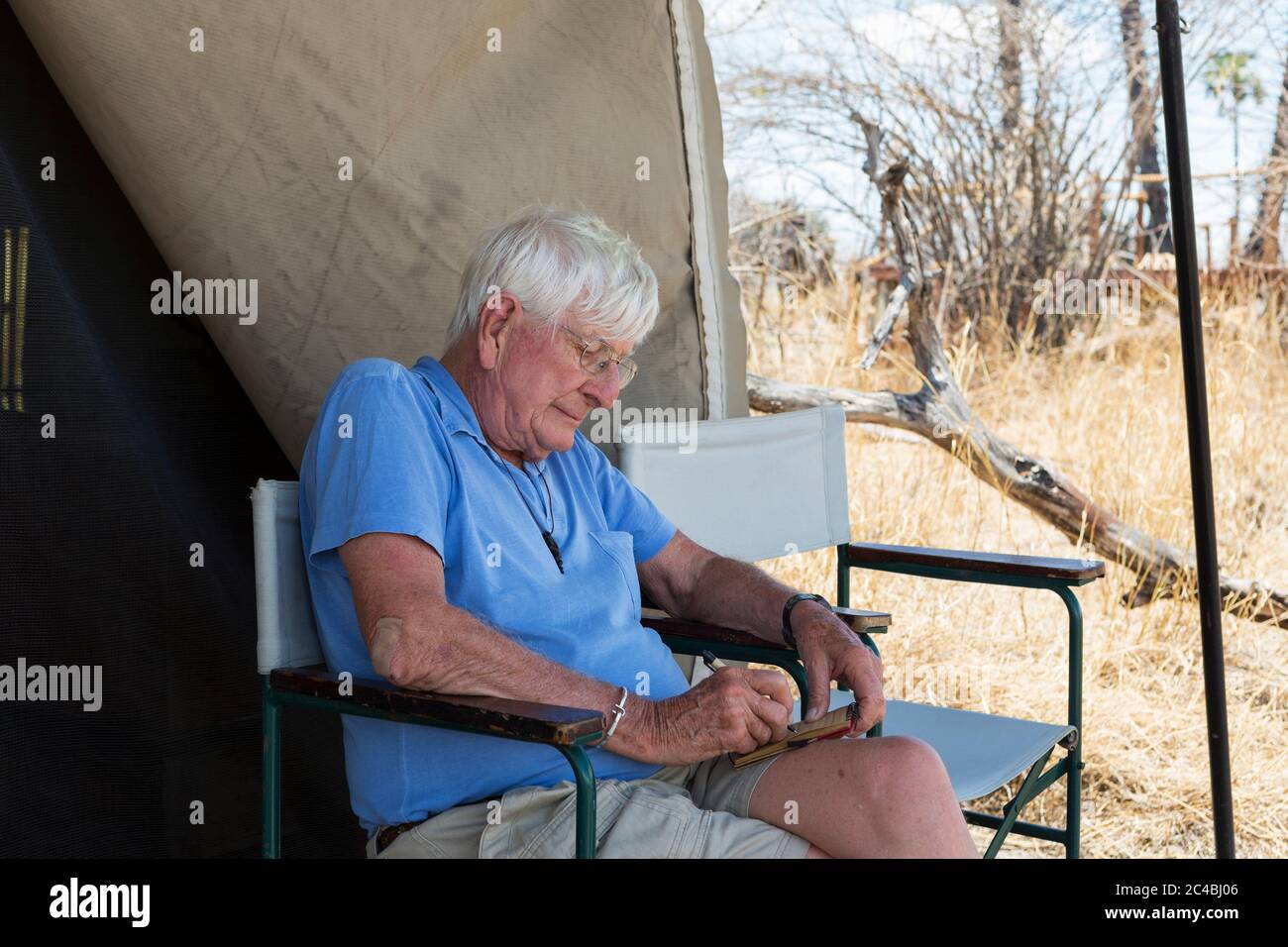 Uomo anziano che scrive un giornale seduto fuori di una tenda in un campo safari della fauna selvatica. Foto Stock