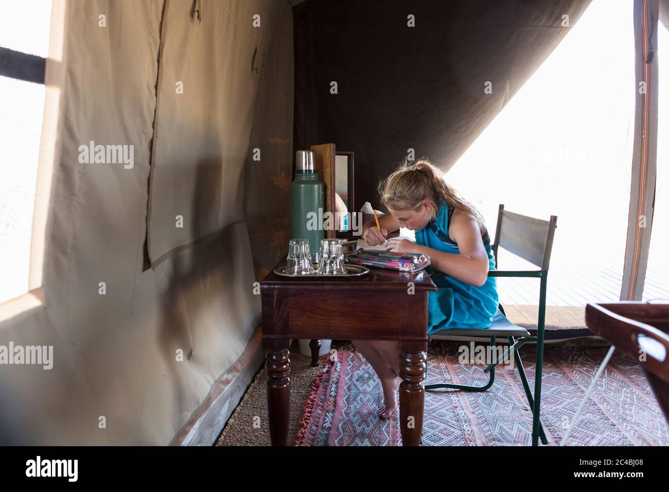 Una ragazza di dodici anni seduta su una scrivania in una tenda in un campo di riserva naturale, disegnando. Foto Stock