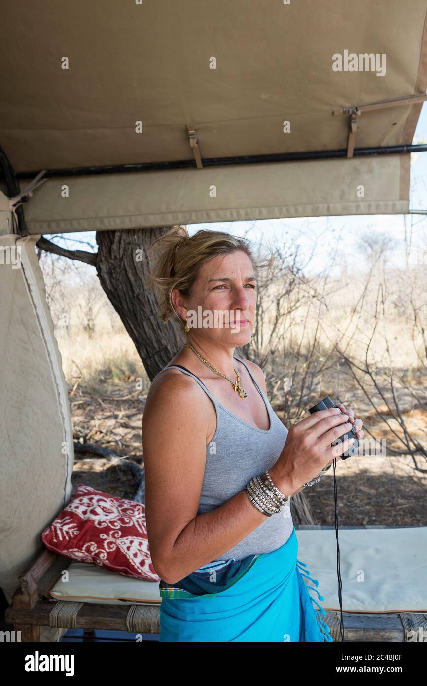 Donna matura da una tenda in un campo di riserva naturale che tiene binocoli Foto Stock