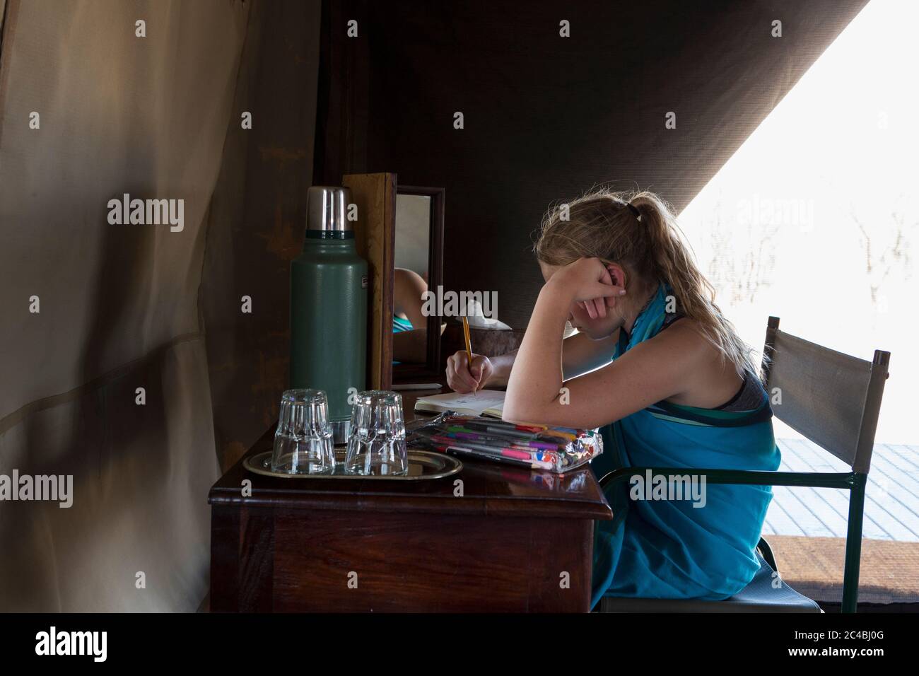 Una ragazza di dodici anni seduta su una scrivania in una tenda in un campo di riserva naturale, disegnando. Foto Stock