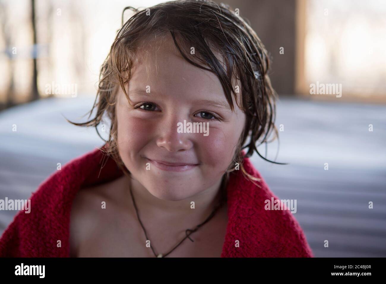 Un ragazzo di cinque anni con capelli bagnati e un asciugamano rosso, sorridente. Foto Stock