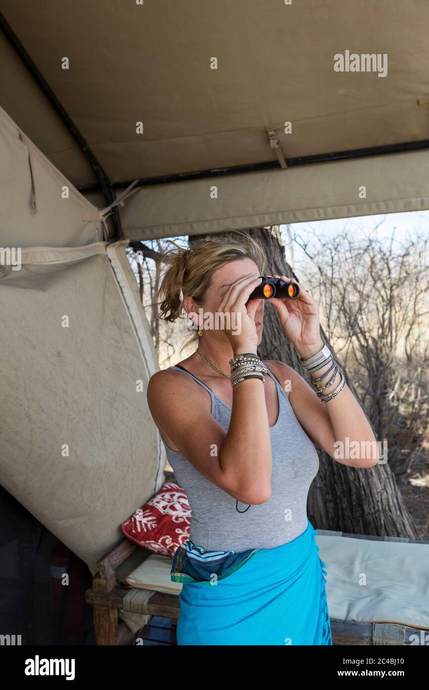 Donna matura da una tenda in un campo di riserva naturale utilizzando binocoli. Foto Stock