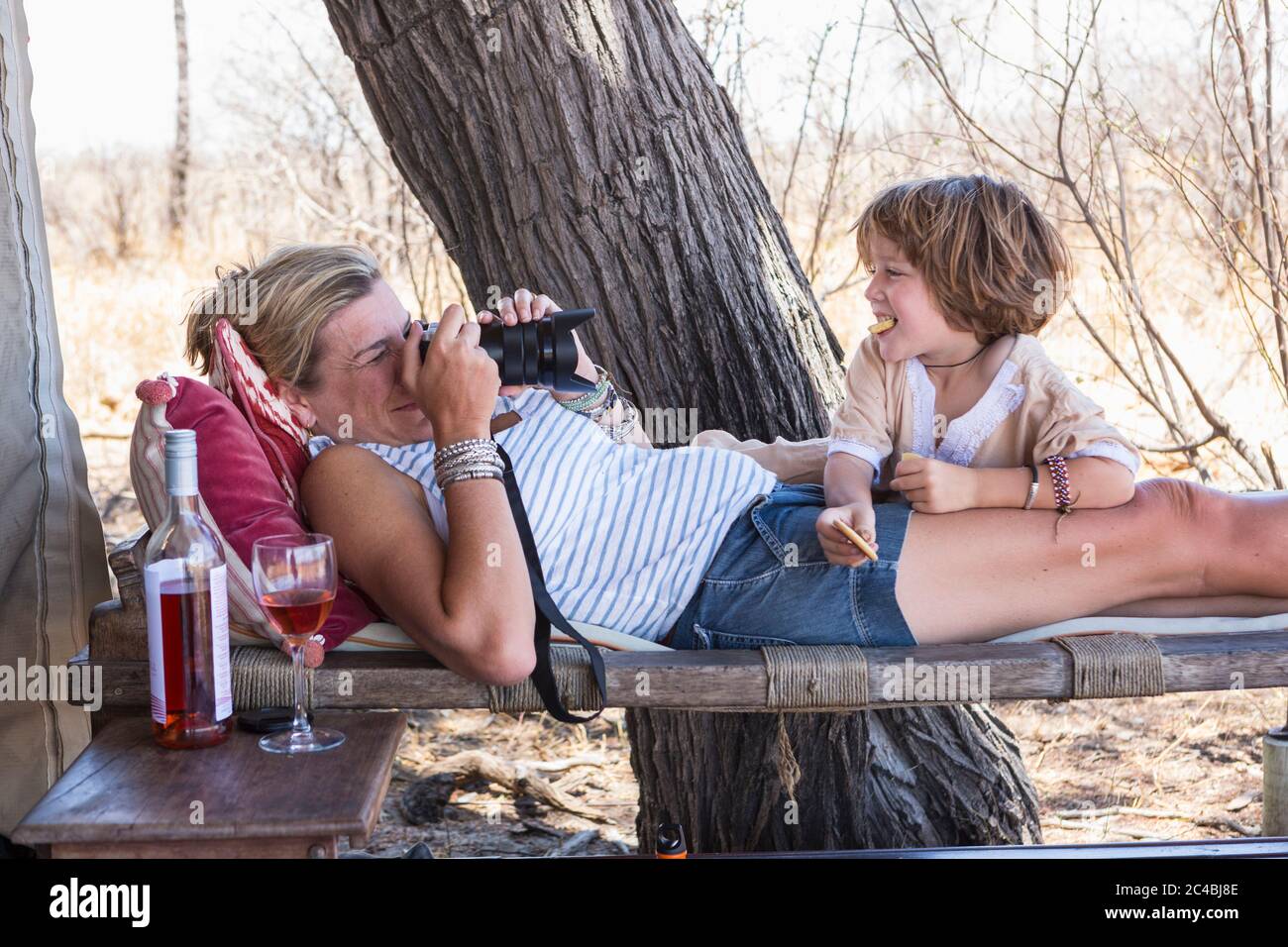 Madre scattando foto del suo figlio di cinque anni, rilassandosi all'ombra di una tenda in un campo safari. Foto Stock