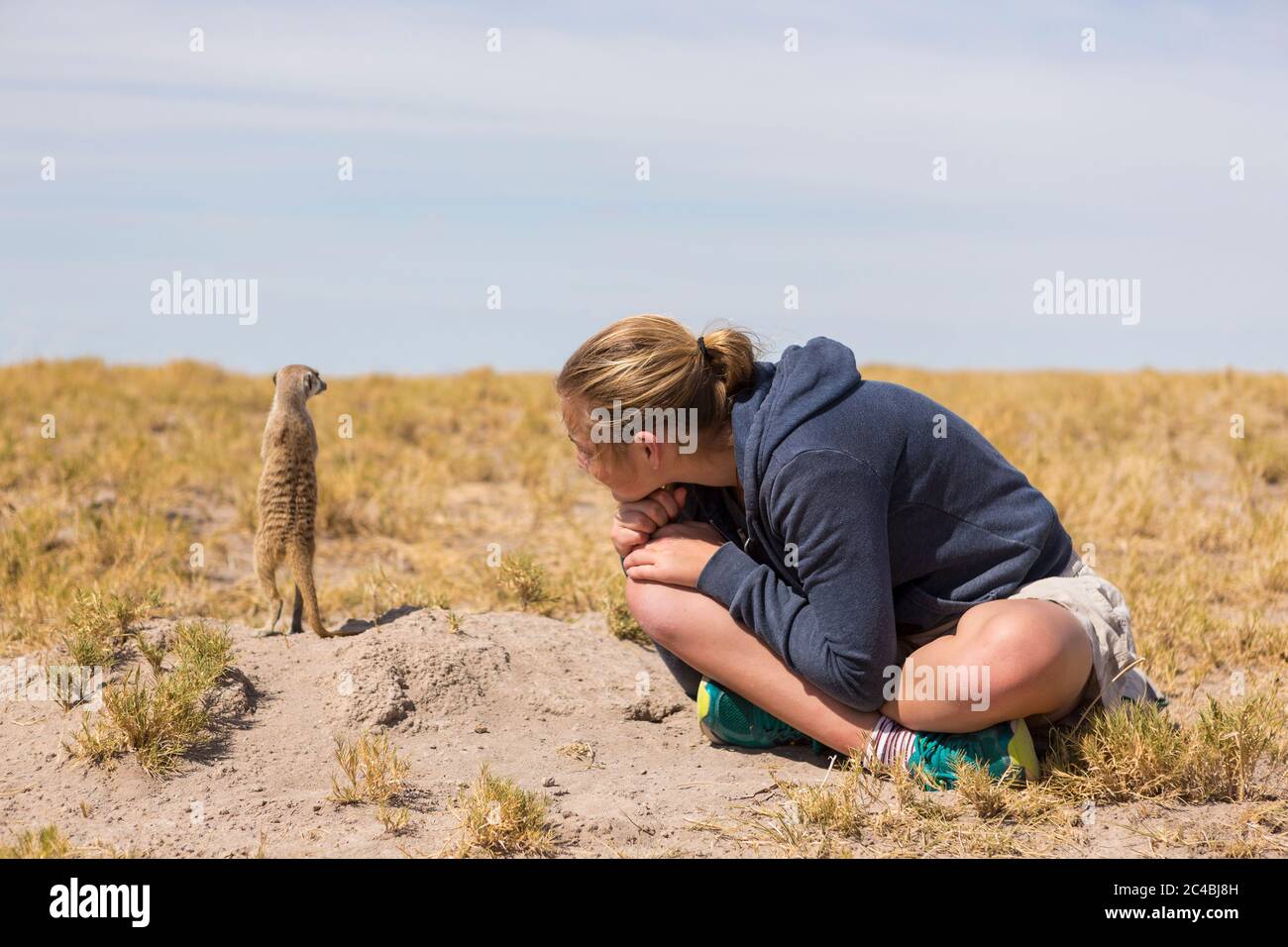 12 anni, seduta a guardare i maerkat uscire dai loro burrows, nel deserto di Kalahari. Foto Stock