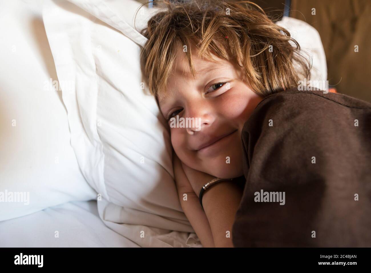 Un ragazzo di 5 anni sorridente a letto nella sua tenda, il deserto di Kalahari. Foto Stock