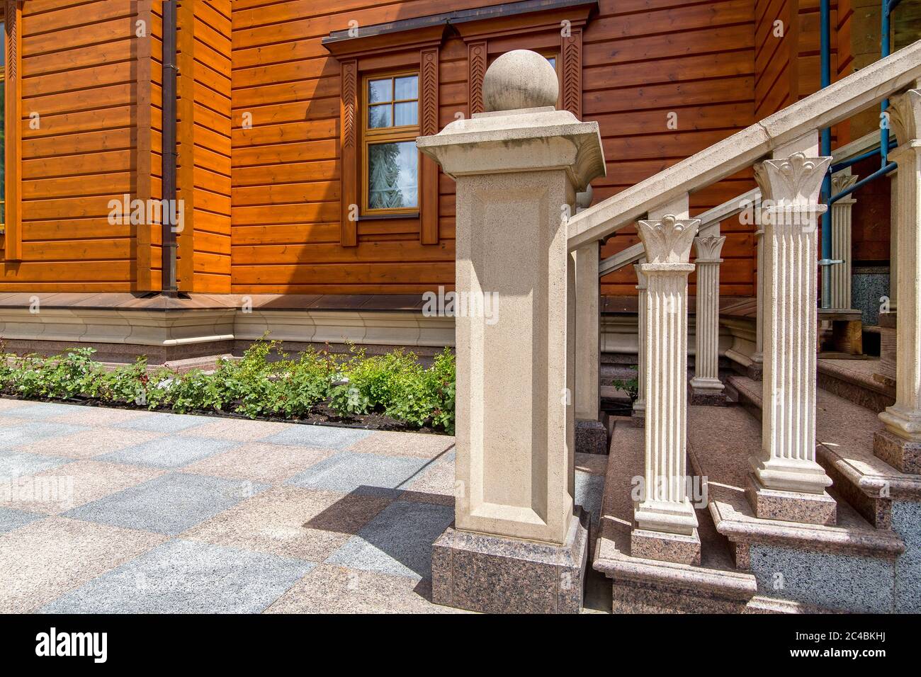 casa in legno con scala in pietra con ringhiera e marciapiede in granito con letto a fiori. Foto Stock