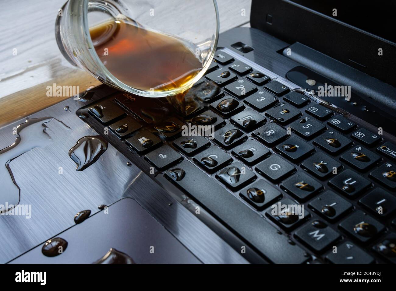Il caffè viene versato accidentalmente sul computer portatile. La tastiera è piena di liquidi e il computer è rovinato. Foto Stock