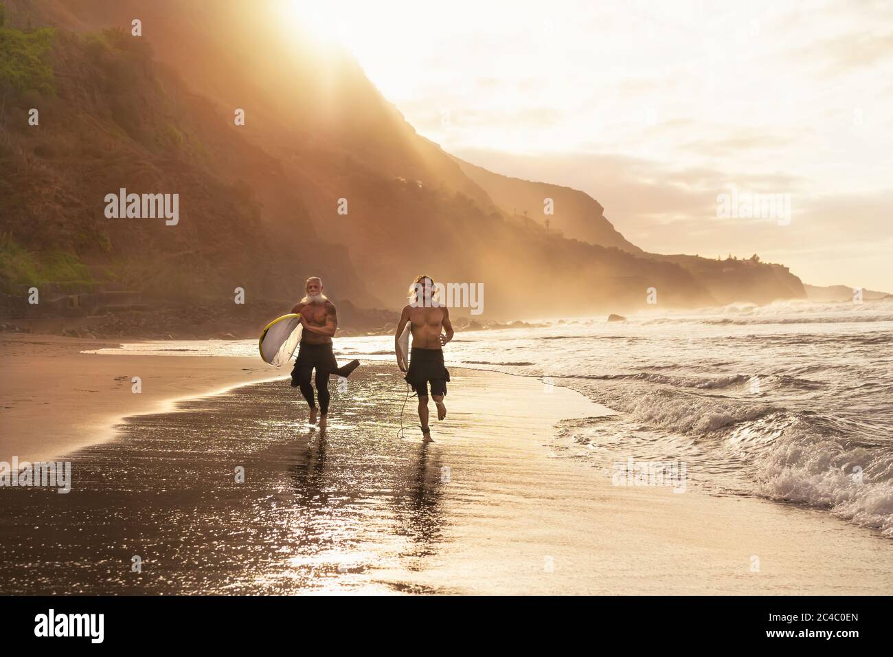 Felici surfisti che corrono sulla spiaggia con tavole da surf - amici sportivi surf e allenamento in vacanza sulla costa tropicale Foto Stock