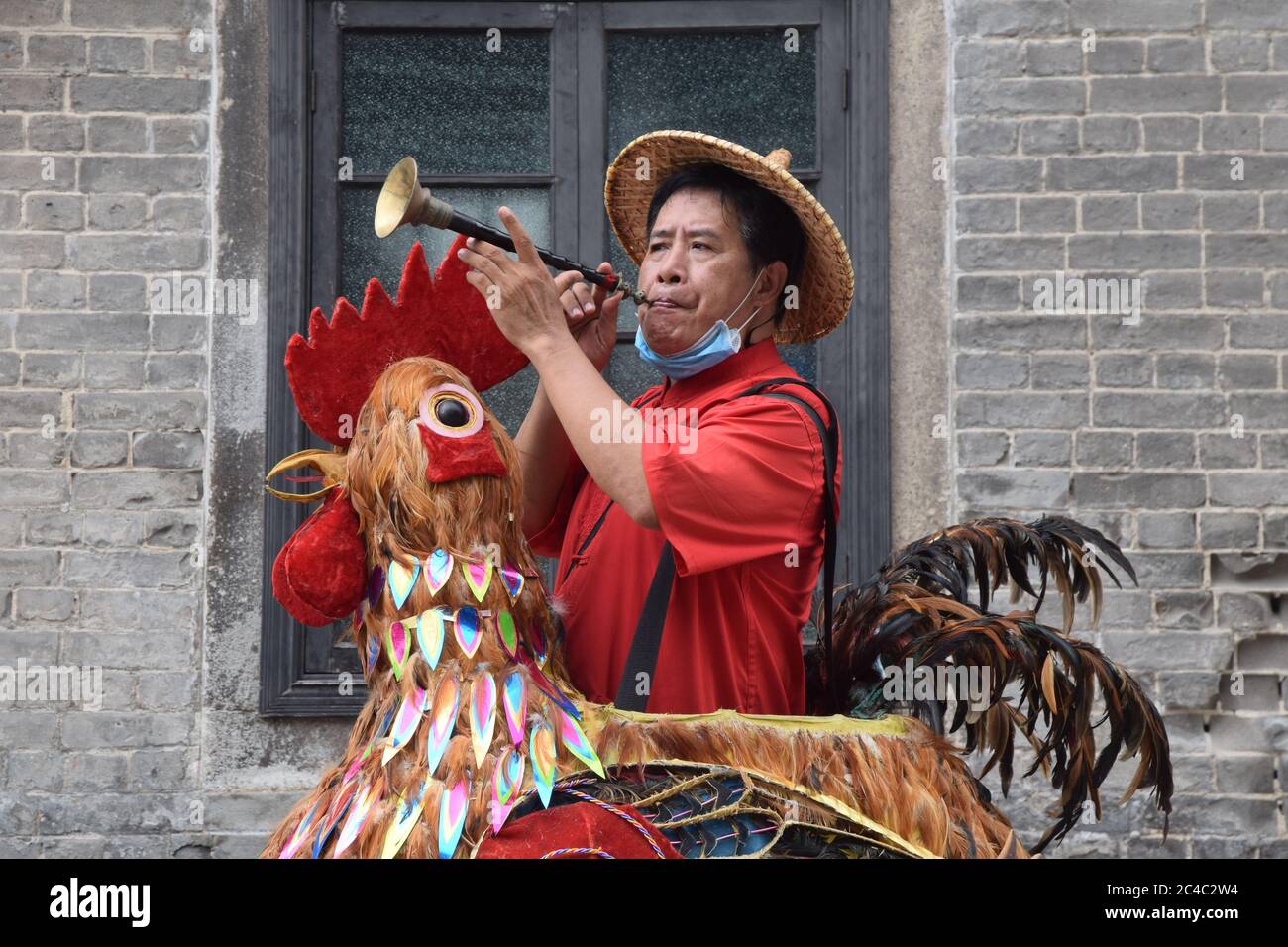 GUANGZHOU, CINA – CIRCA GIUGNO 2020: Il venditore di strada a Guangzhou si è vestito come un gallo colorato che soffia in un corno per vendere olive cinesi sottaceto. Foto Stock