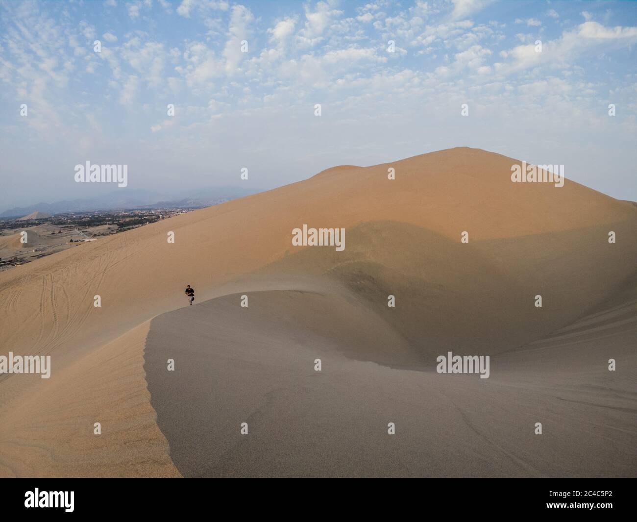 giovane uomo che sale una duna nel deserto, nuvole e cielo blu Foto Stock